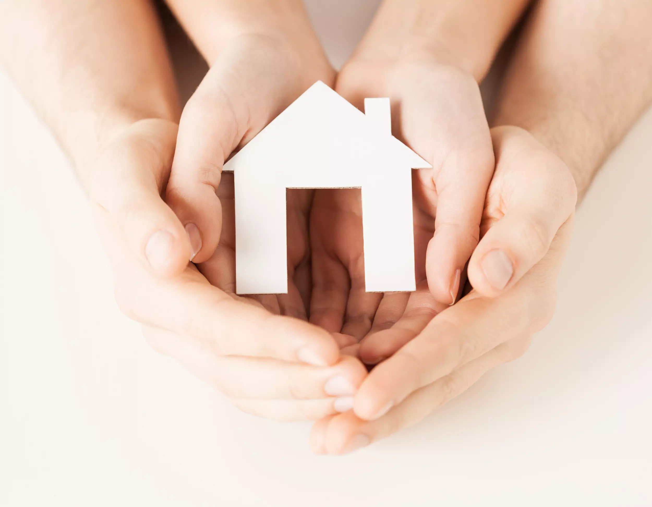 A family of hands holding a white house cutout